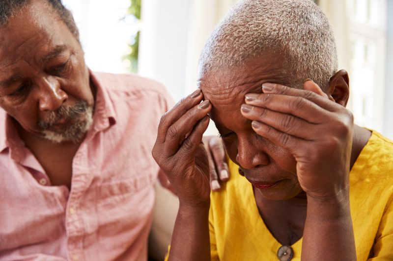Sinais e sintomas do Alzheimer - idosa com a mão na cabeça, sendo amparada por homem