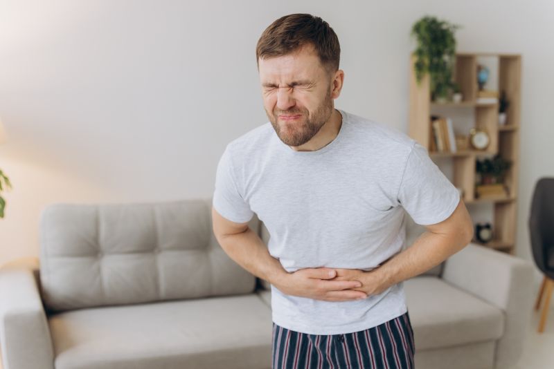 Homem com a mão na barriga, indicando sentir dores/cólicas, um dos sintomas da virose gastrointestinal.